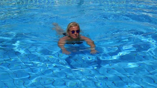 Белокурая дама плавая в бассейне на матрасе занимается мастурбацией 