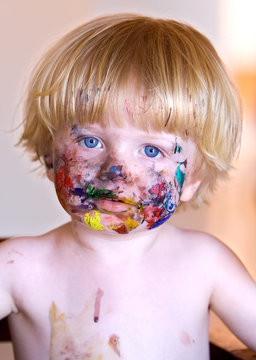 young boy with face covered in colourful paint