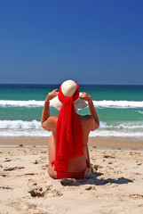girl sitting on sandy beach in the sun adjusting hat. blue sky,