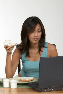 Asian Woman Eating Bagel At Computer