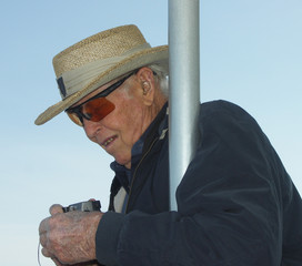 Senior citizen man, wearing a hat and sunglasses, tourist, getting his camera out, supporting himself with a pole