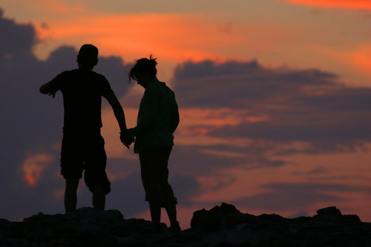 silhouette of couple walking in front of sunset