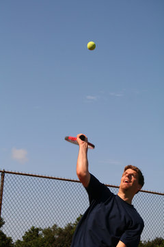 young man serving tennis ball
