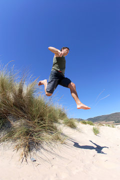 Fit, Healthy Middle Aged Man Leaping Over Sand Dunes