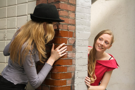 Two Girls Peeking Around The Wall