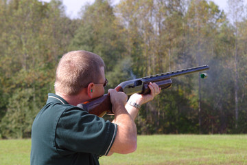 busting clays at an outdoor range with a shotgun and hulls flying with smoke