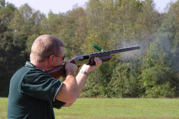 sporting clays shoot who has just touched off a shot from his shotgun that has the empty shell coming out and smoke at the barrel