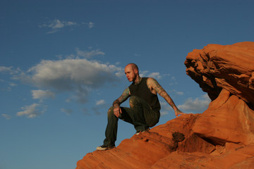 tattooed man sitting on the red rocks