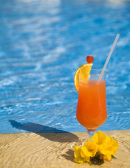 orange cocktail stands on edge of pool.