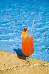 orange cocktail stands on edge of pool.