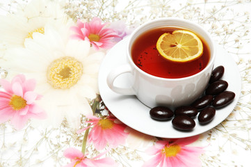tea with lemon and chocolates on floral background