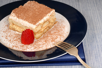 a piece of tiramisu dusted with cocoa with a fork on a blue plat