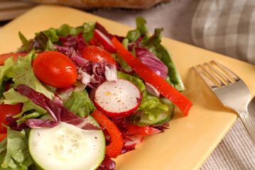 a crisp healthy salad with a fork on a yellow plate with rustic