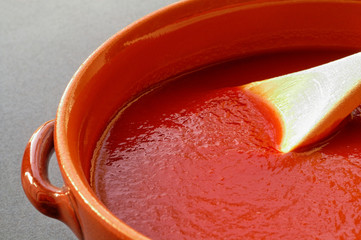 terracotta pot and wooden spoon with tomato sauce.