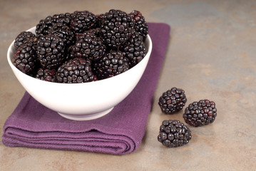 blackberries in a white bowl on a purple napkin with blackberrie