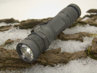 Tactical flashlight with an all-aluminum body resting on rocks with a dusting of snow in the...