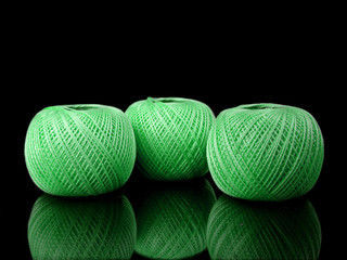 three balls of green string on a black background with reflectio