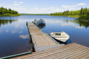 two boats docked on a peaceful lake on a sunny day with trees and blue water behind