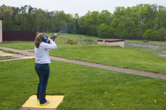 Woman at a clays shooting range using a shotgun to break targets. 