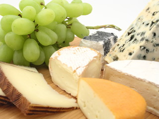 Käsebrett mit einer Vielzahl von Käse und frischen grünen Trauben freigestellt auf weißem...