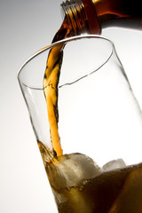cola pouring into glass with ice