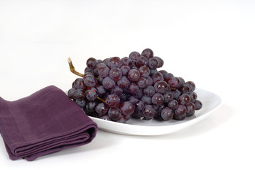 a bunch of juicy red grapes on a white plate with a purple napki