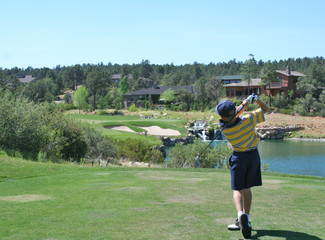 young golfer hitting a shot over a water hazard
