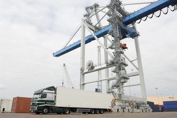 truck in port waiting beneath large crane
