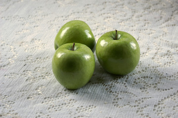 three granny smith apples on lace