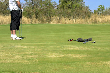 golfer standing on the green with two golf clubs.