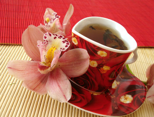 red cup of tea in the form of heart with pink orchids over straw