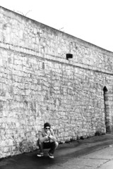 junger mann hockt vor steinmauer