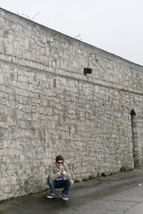 junger mann hockt vor steinmauer