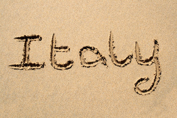italy, written on a sandy beach.