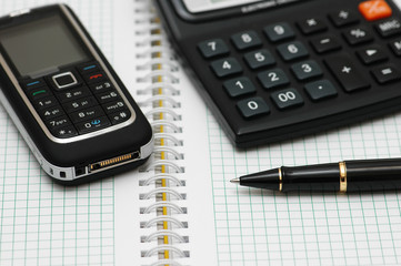 mobile phone, calculator and pen on the notebook