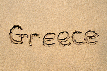 greece, written on a sandy beach.