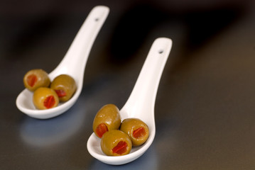 stuffed green olives in two white spoons