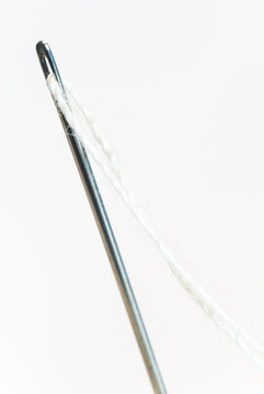 needle with white cotton thread threaded through eye isolated on