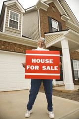 middle-aged woman holding a for sale sign.