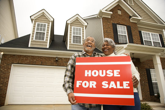 middle-aged couple holding a for sale sign.