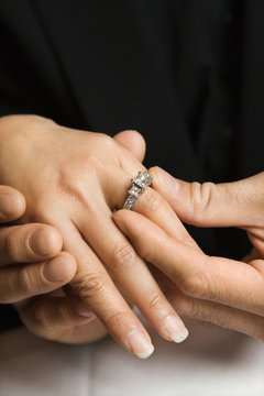 Adult male putting  ring on female's hand.