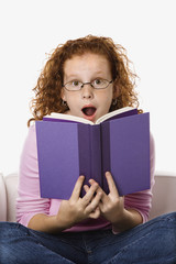 Girl sitting reading book looking surprised.