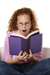 Girl sitting reading book looking surprised.