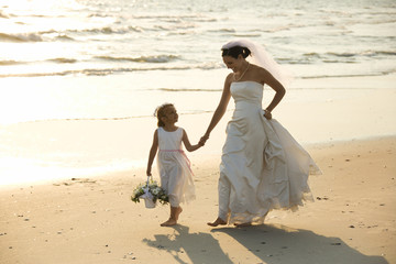 Bride and flower girl walking on beach.