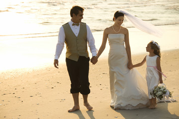 Bride, groom and flower girl walking on beach.