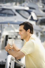 Man holding coffee cup at harbor.