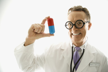 doctor wearing eyeglasses holding an oversized pill.