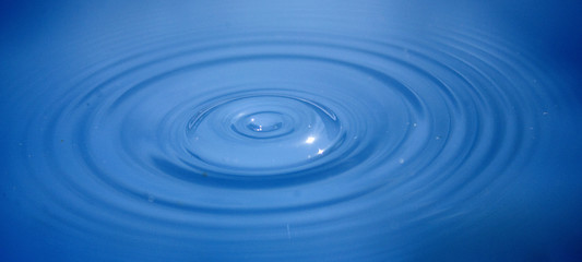 Ripples across blue water seconds after a drop has hit the surface