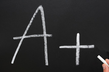 a teacher writing a+ on a blackboard.
