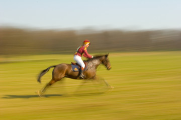 Blurred horse and rider crossing a field during an eventing competition
